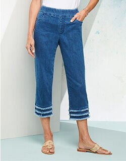 waist-down view of woman wearing blue jean capris with fringe around leg opening