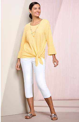 model wearing yellow blouse that ties at waist, and white capris