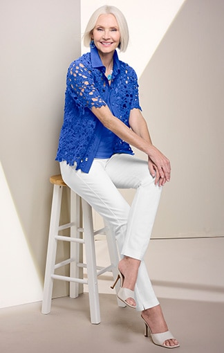 model wearing blue lace top and white pans, sitting on a stool