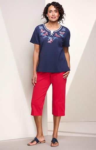 model wearing blue shirt with red, white, and blue pattern around neck, red capris