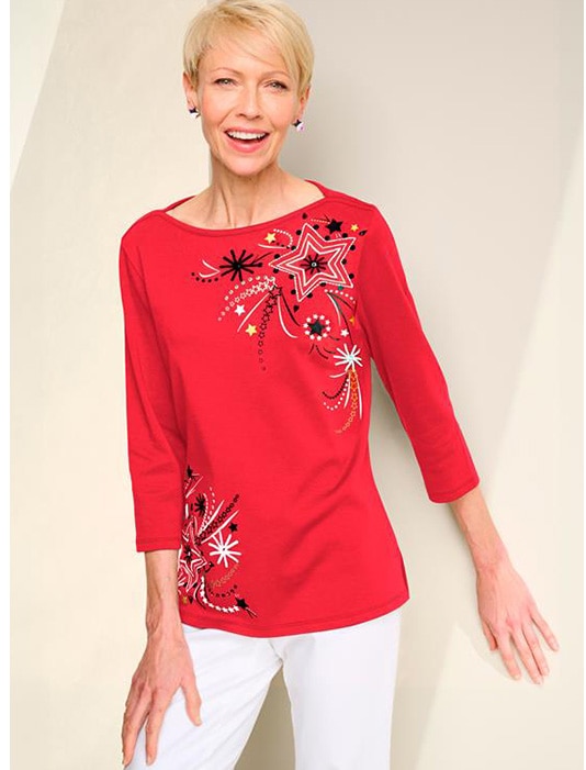 model wearing red patterned top and white pants, smiling into the camera
